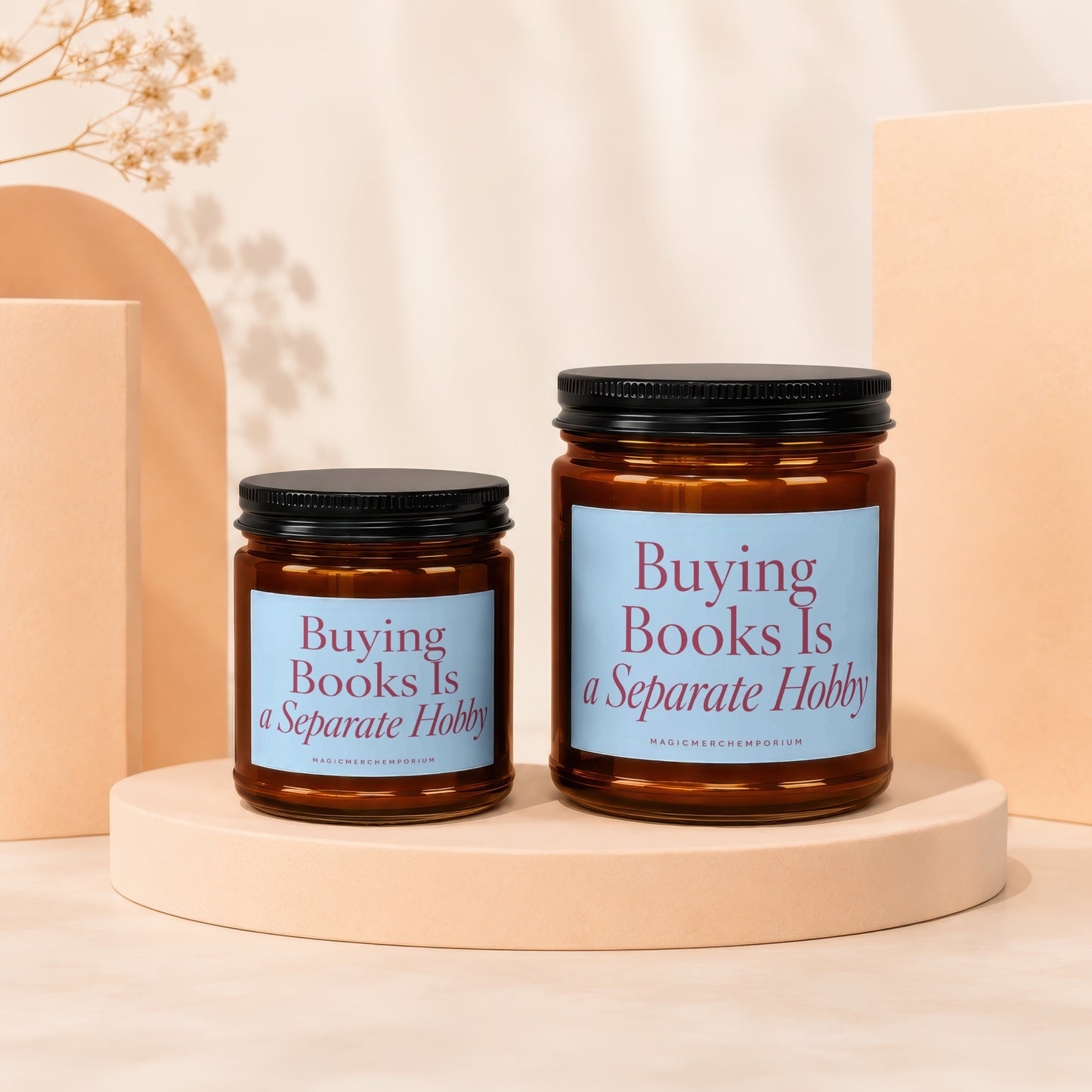 Two amber glass candles with black lids and pale blue labels reading "Buying Books Is a Separate Hobby."
