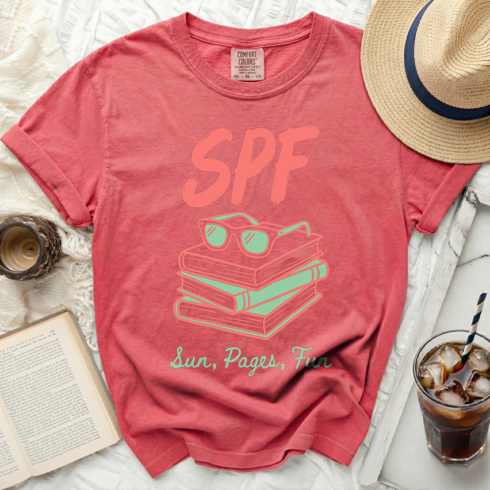 Coral t-shirt with sunglasses and books graphic and text "SPF Sun, Pages, Fun".
