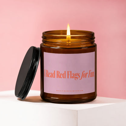 Amber jar candle with a lit flame and a black lid, featuring pink label text "I Read Red Flags for Fun."