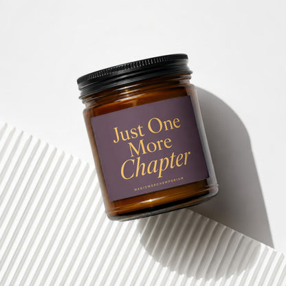 Amber glass candle with a dark purple label that reads "Just One More Chapter."