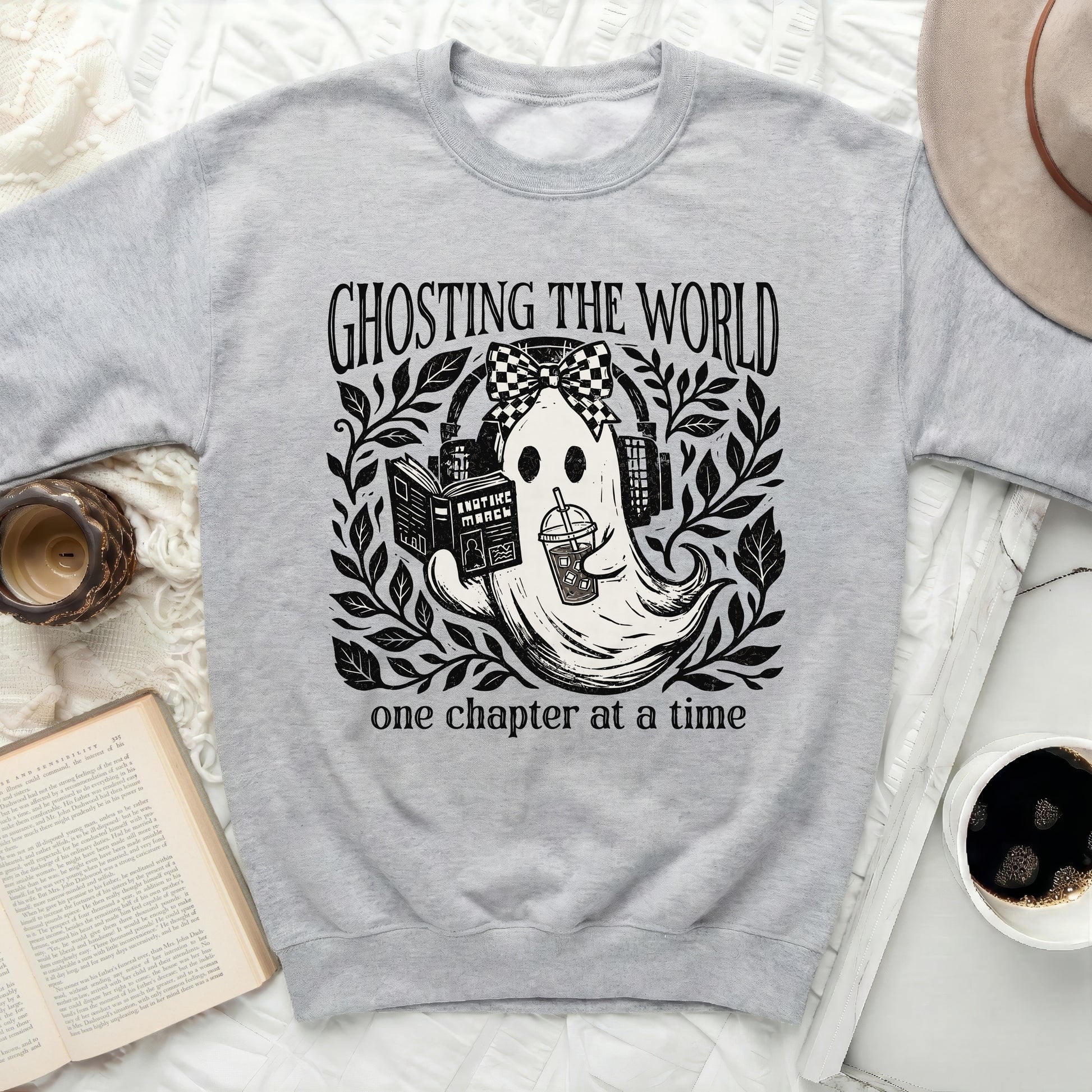 Grey sweatshirt with a graphic of a ghost reading and drinking, with text "GHOSTING THE WORLD one chapter at a time".
