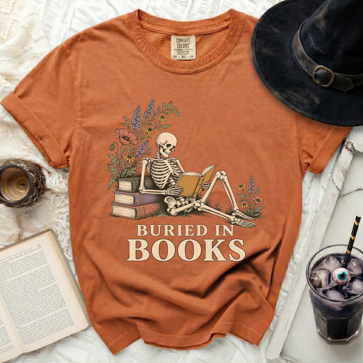 Orange t-shirt with skeleton reading a book and text "BURIED IN BOOKS".