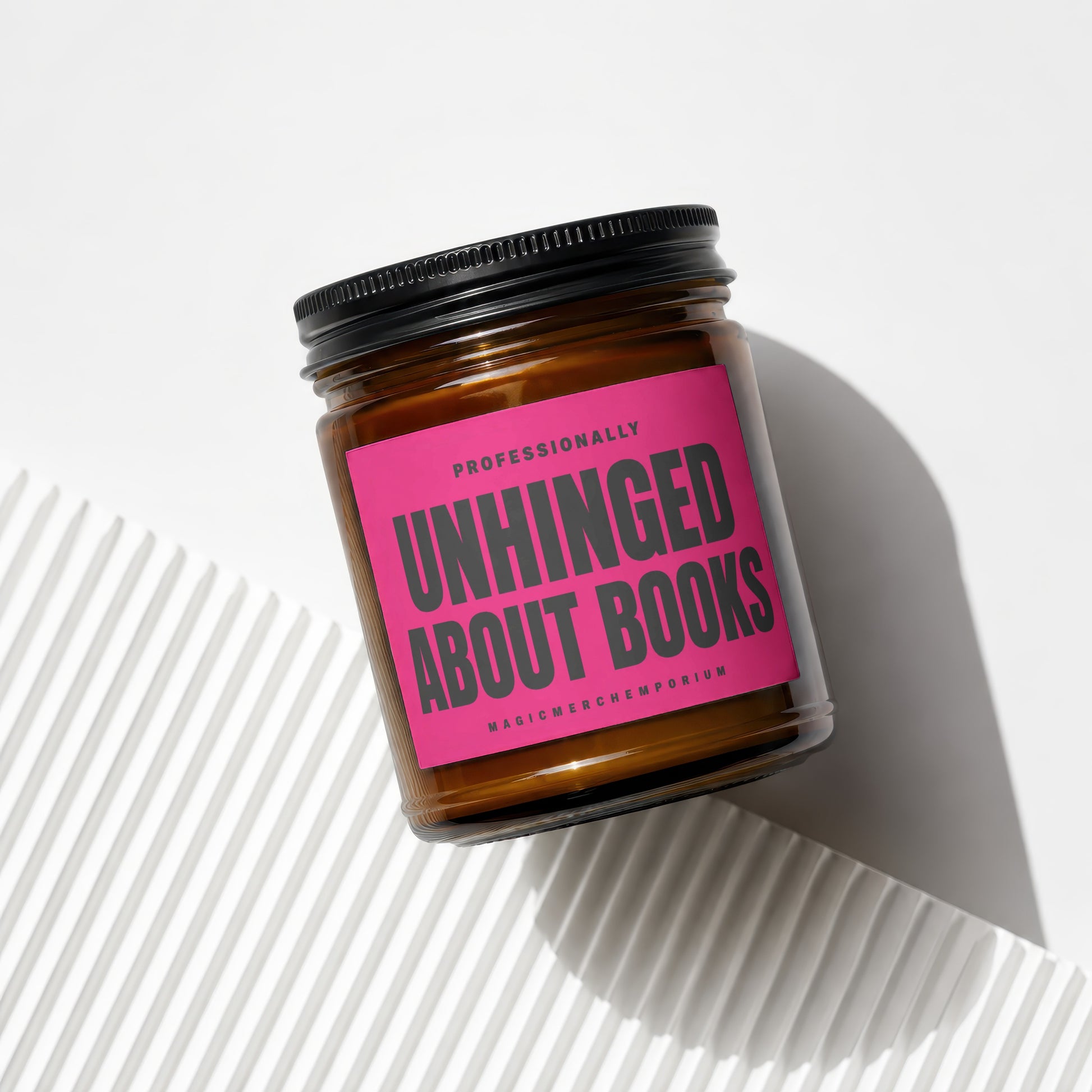 Amber jar candle with pink label reading "Professionally Unhinged About Books".