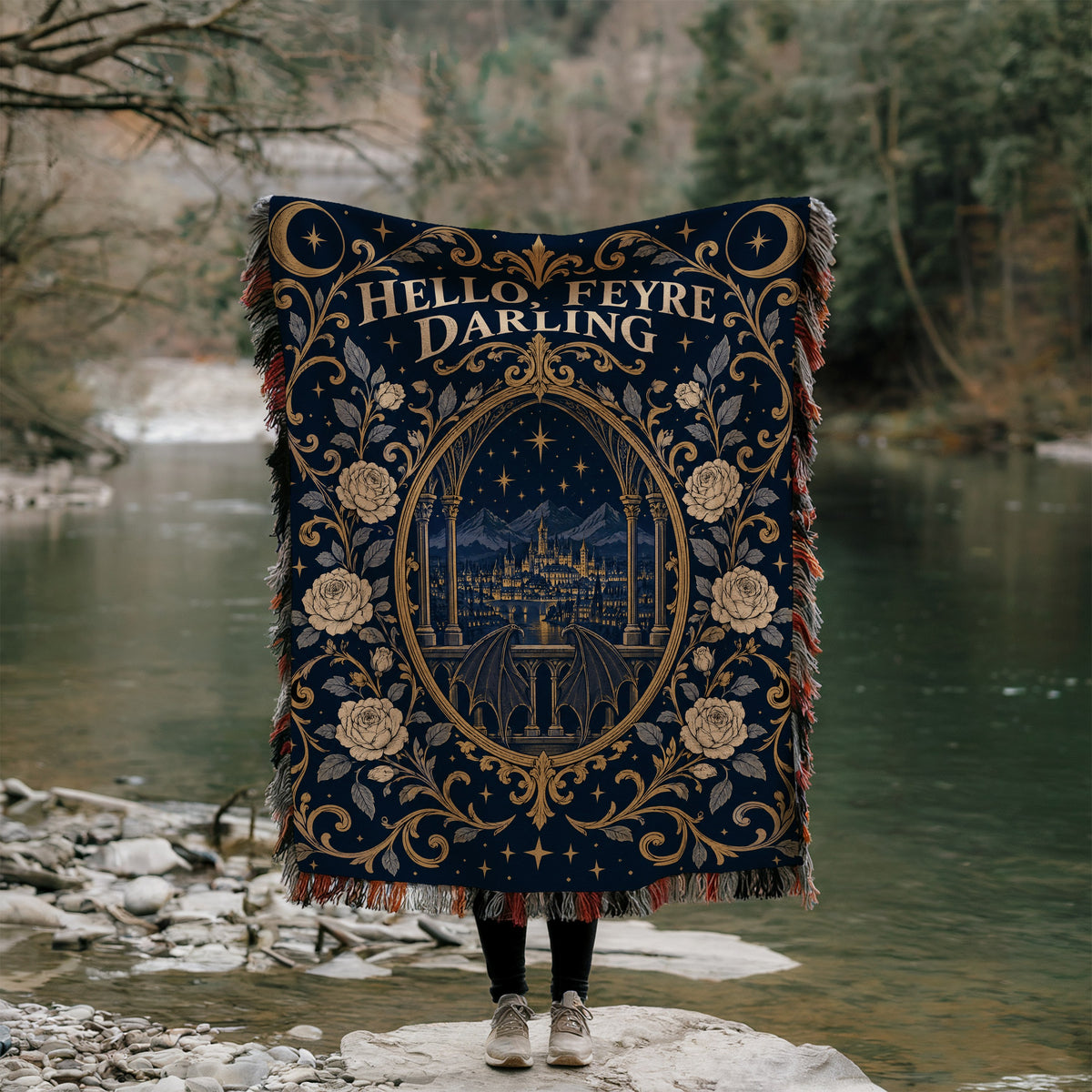 Hello Feyre Darling Crest Woven Throw Blanket held up by a river