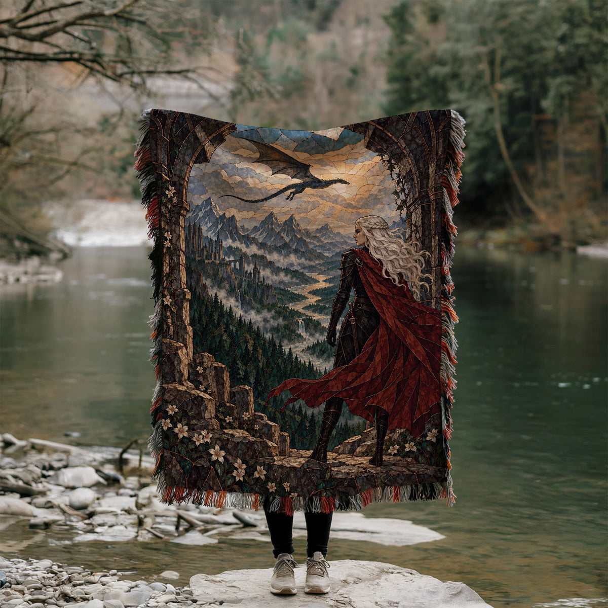 Wyvern at the Mountain Pass Woven Throw Blanket held up outdoors by a river