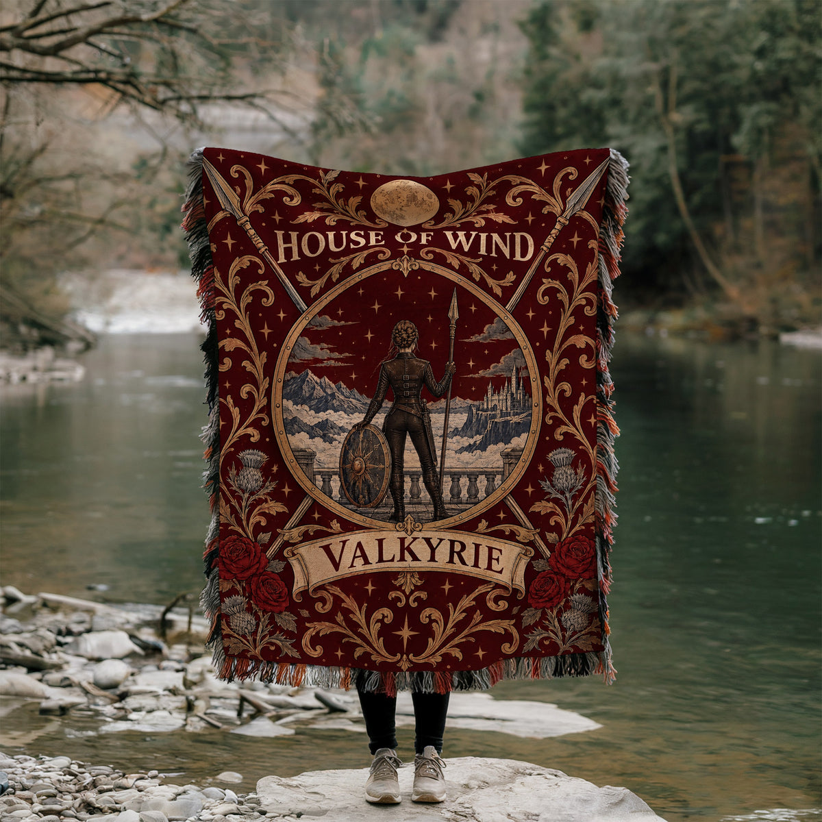 Valkyrie House of Wind Crest Woven Throw Blanket held up by a river