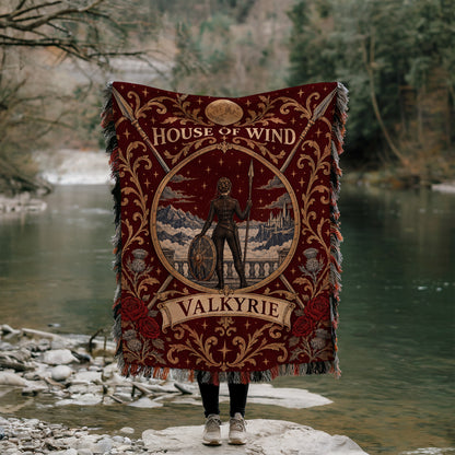 Valkyrie House of Wind Crest Woven Throw Blanket held up by a river