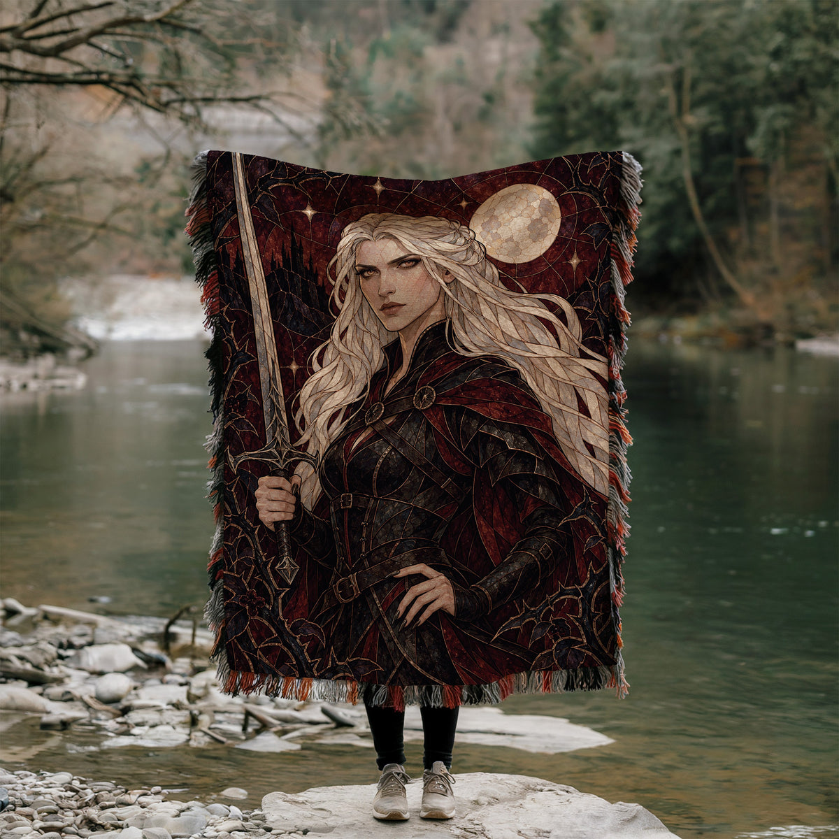 Iron Queen Woven Throw Blanket held up outdoors by a river