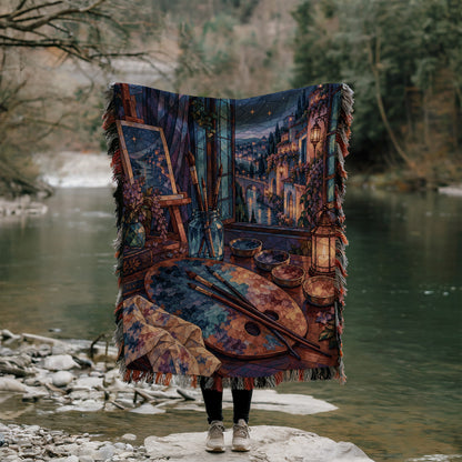 The Rainbow of Velaris Woven Throw Blanket held up outdoors by a river