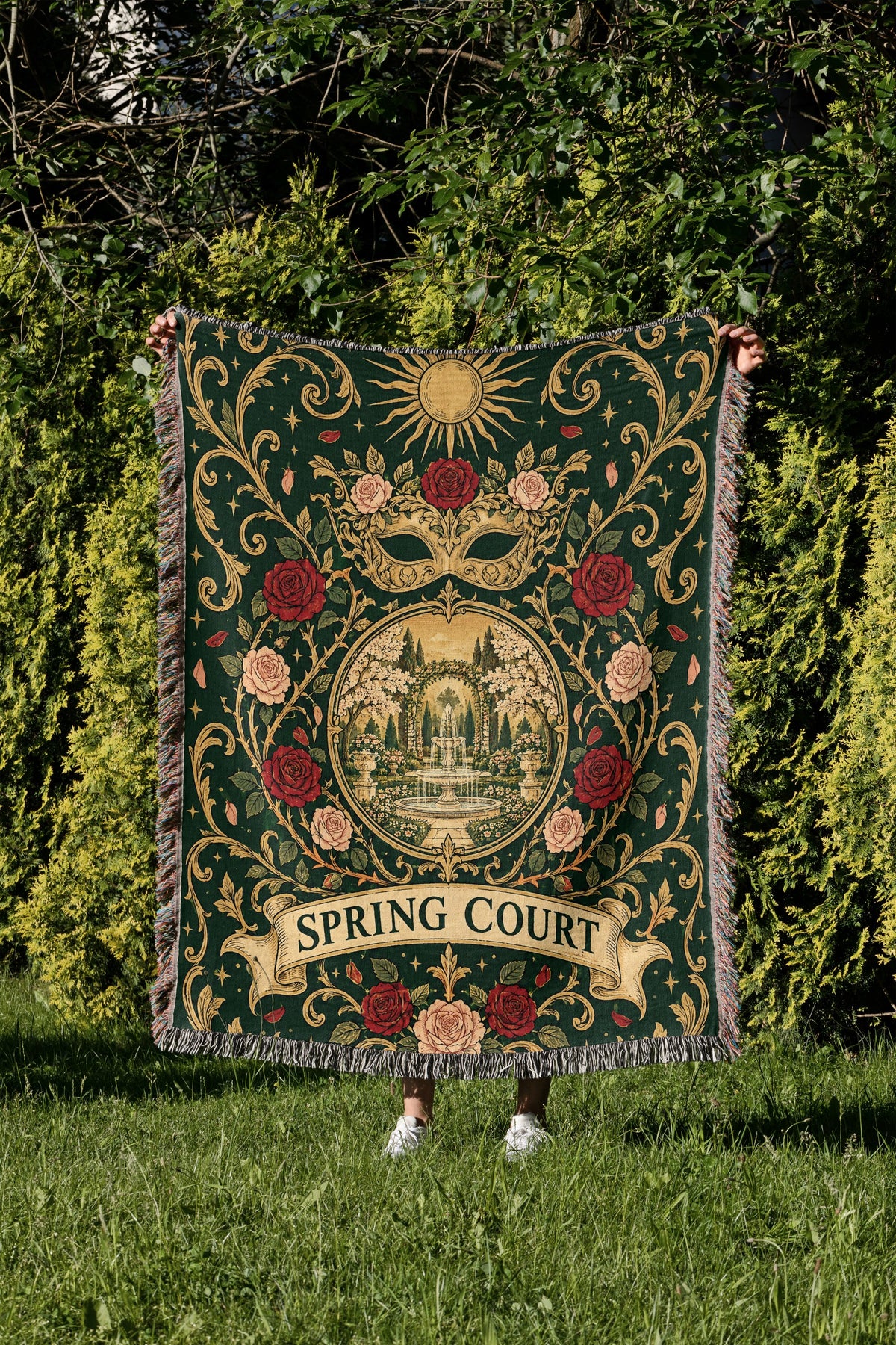 Spring Court Masquerade Crest Woven Throw Blanket held up in a garden