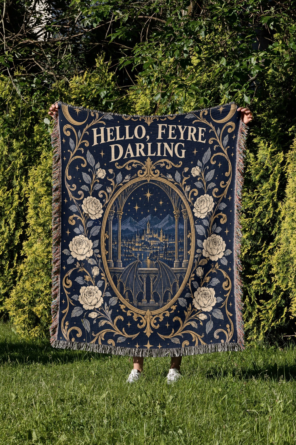 Hello Feyre Darling Crest Woven Throw Blanket held up in a garden