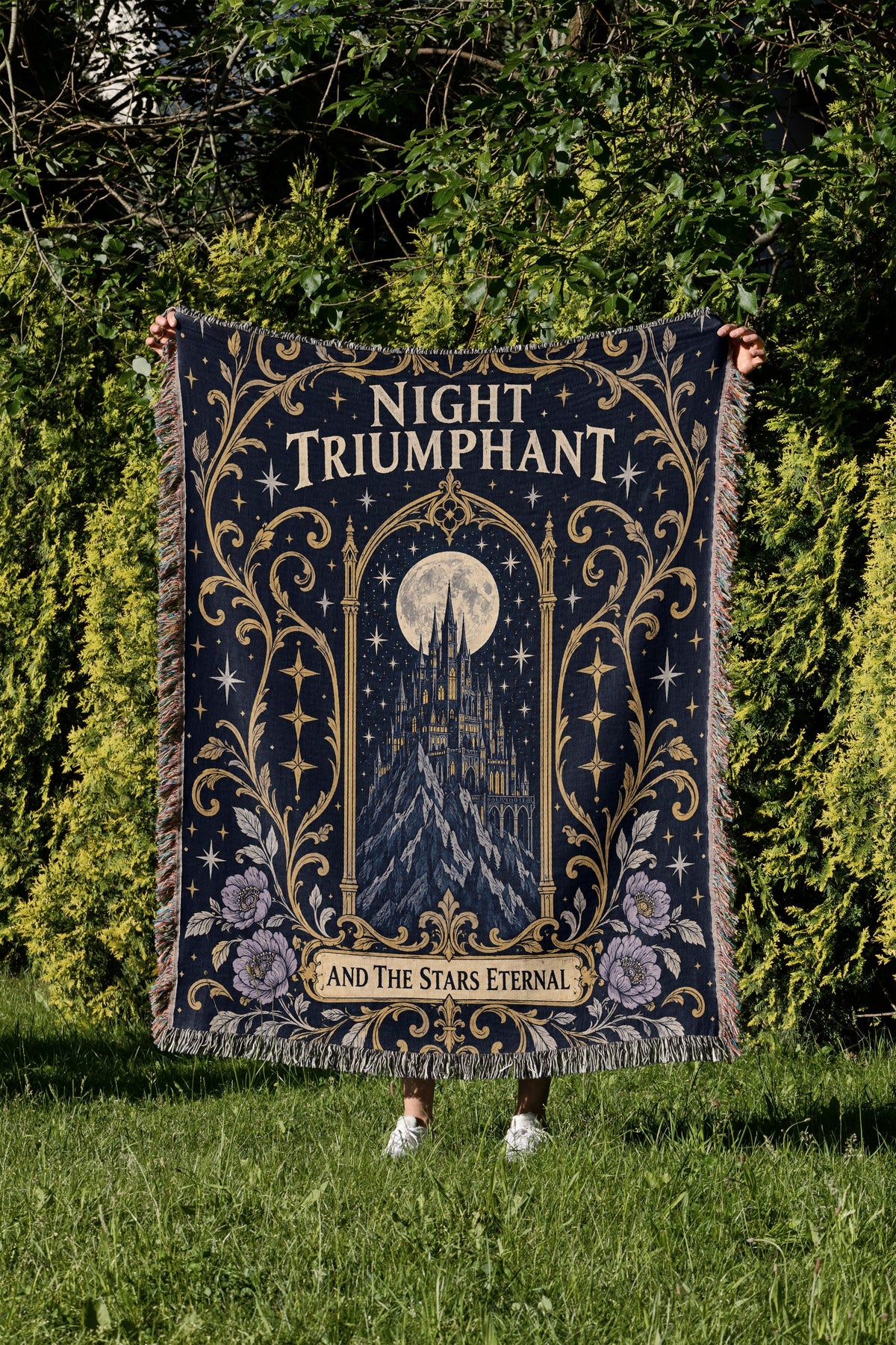 Night Triumphant Crest Woven Throw Blanket held up in a garden