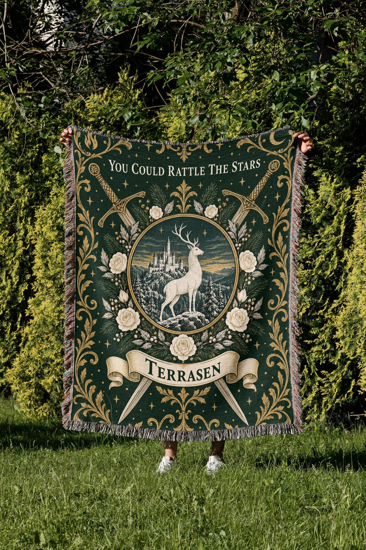 Terrasen Crest Woven Throw Blanket held up in a garden