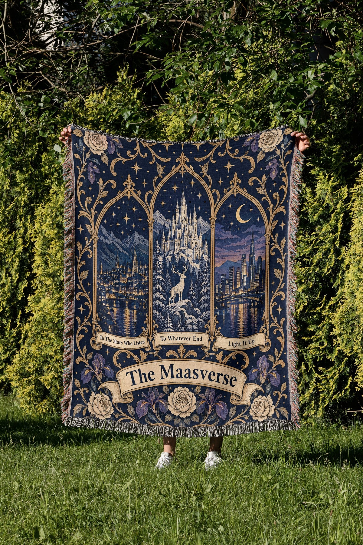 Maasverse Three Realms Crest Woven Throw Blanket held up in a garden