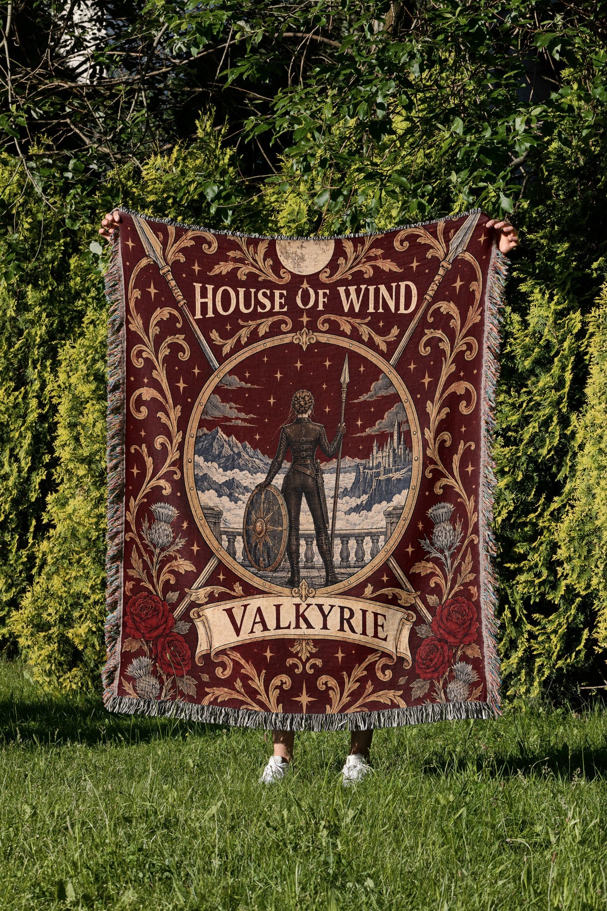 Valkyrie House of Wind Crest Woven Throw Blanket held up in a garden