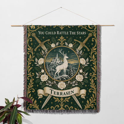 Terrasen Crest Woven Throw Blanket hanging on a wall with a plant