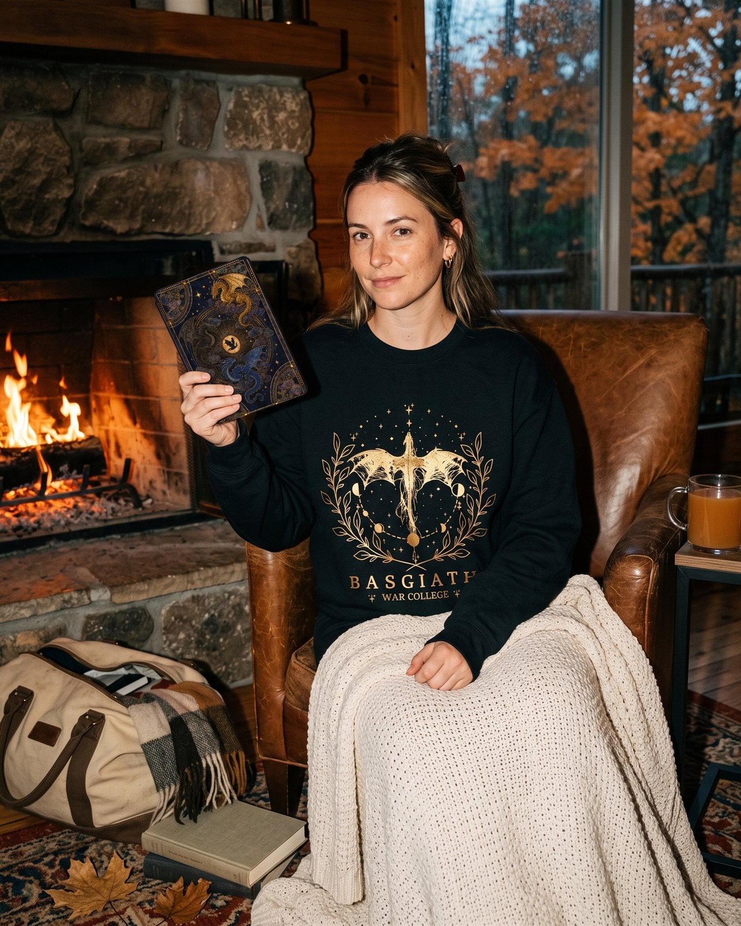 Reader by a cabin fire in the Basgiath War College sweatshirt, holding a Kindle in the Fourth Wing stained glass dragon case